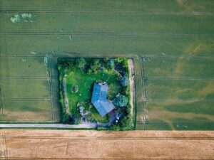 Rural house nestled between green and golden crop fields.
