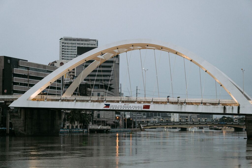 A view of a modern arch bridge spanning over the Pasig River in Manila during daytime.