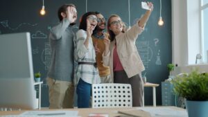 Diverse team of young professionals taking a selfie in a modern office setting.