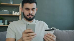 A man using a smartphone and credit card for online shopping at home.