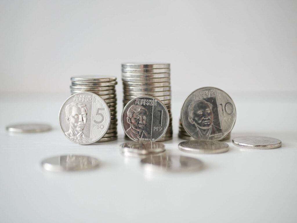 Stacked and scattered Philippine Peso coins in a close-up view on a white surface.